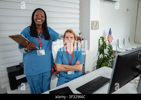 Diverse nurses standing together smiling in medical reception area Stock Photo