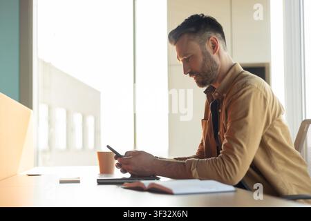 Focused Caucasian Male Using Smartphone At Modern Office Desk, Business Concept Stock Photo