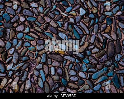 Top-down view of smooth polished pebbles embedded in concrete, featuring a mix of blue, grey, and earthy tones. Ideal for textures and backgrounds. Stock Photo