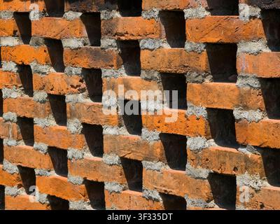 Close-up of a red brick wall with a geometric pattern of open ventilation holes and strong shadows. Perfect for architectural backgrounds. Stock Photo