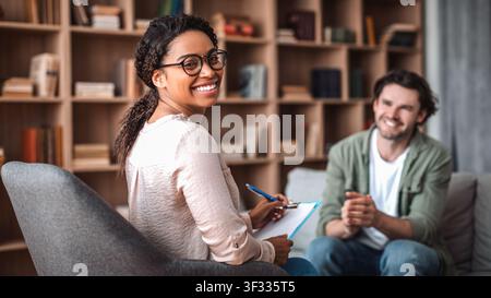 Smiling Young Black Woman Taking Notes During Counseling Session, Office Environment Stock Photo