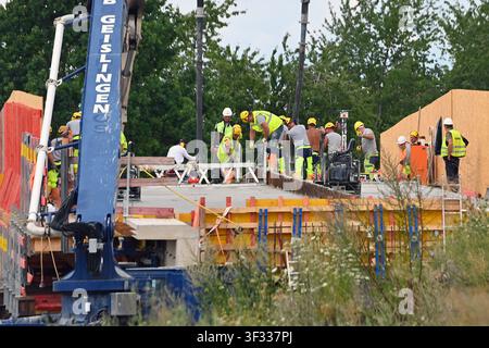 Construction workers concrete the road surface during the new construction of a bridge. Active large-scale construction site for the new construction of a bridge. A group of construction workers in clearly visible work clothing, consisting of neon yellow w Stock Photo