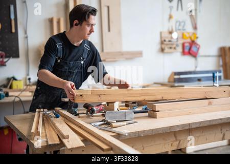 Working progress in carpentry workshop, concentrated man restorer choosing selecting wooden planks. Stock Photo