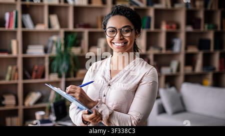 Smiling African American Woman Holding Clipboard In Modern Office, Business Concept Stock Photo