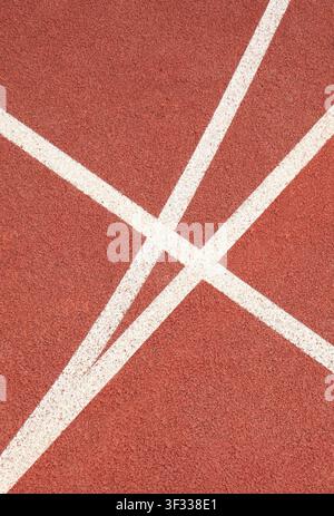 Abstract overhead view of white painted directional lines intersecting on a red rubber athletic running track. Featuring a clean geometric pattern. Stock Photo