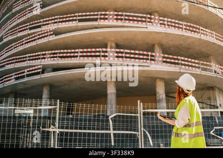 Female construction worker in hard hat and safety vest checking a construction site Stock Photo