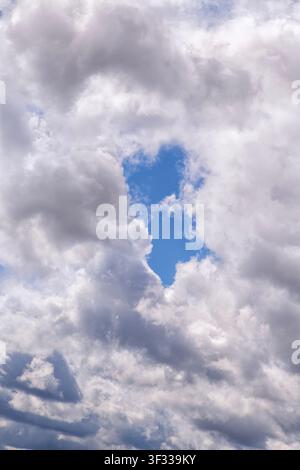 Vertical dramatic sky with thick gray storm clouds surrounding a narrow vivid blue opening. Moody atmospheric scene symbolizing hope amid darkness. Id Stock Photo