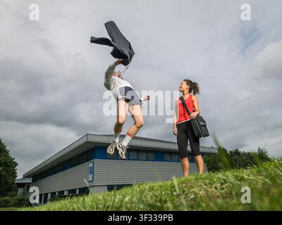 Man jumping in air as couple walk away from office wearing sportswear Stock Photo