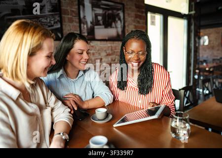 Diverse women friends smiling using digital tablet in cafe Stock Photo
