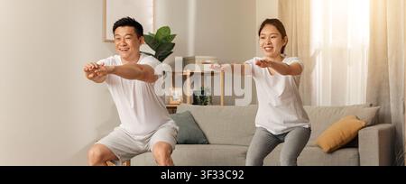 Happy Asian Couple Exercising Together At Home, Doing Squats. Fitness Concept Stock Photo