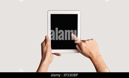 Young man touching blank screen of tablet computer on light background, close up. Mockup for design. Panorama Stock Photo