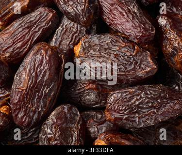 pile of dark brown medjool dates in full frame, sweet dried fruit with wrinkled skin and sticky texture, taken from above close-up view Stock Photo