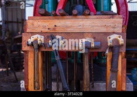 Collection of old hammers and workshop tools hanging on a wooden storage rack, reflecting traditional craftsmanship and industrial heritage in a worki Stock Photo