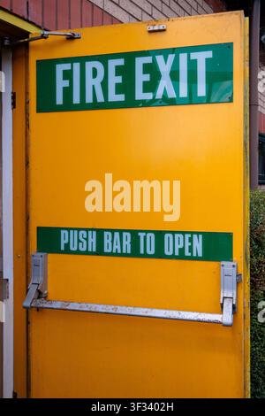 Fire exit door with a clear green sign on a bright yellow background, featuring a 'FIRE EXIT' message and a push bar for emergency egress, ensuring bu Stock Photo
