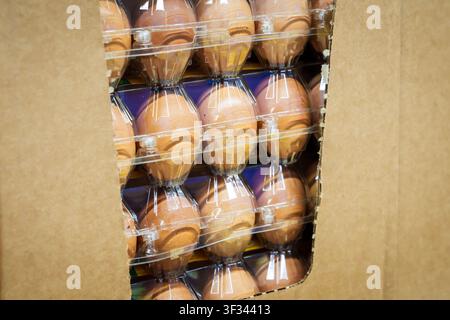 RIGA, LATVIA. 12th March 2026. Fresh brown chicken eggs packed in transparent plastic cartons stacked inside a cardboard box on a store shelf. Stock Photo