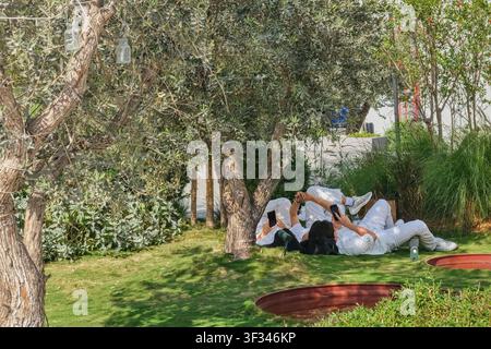 Employees enjoy outdoor break in landscaped public spaces, reflecting Dubai's work-life balance, people-friendly city environment. Stock Photo