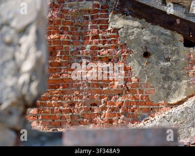A crumbling old red brick wall with weathered grey plaster and exposed concrete debris. Stock Photo