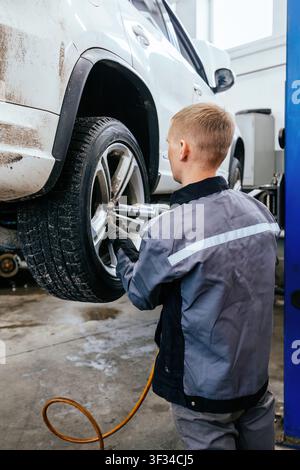 Changing car tire and wheel in auto service using pneumatic wrench. Stock Photo