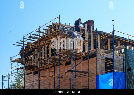 Construction worker rebuilding a historic timber roof on scaffolding during restoration of a heritage building with structural repairs Stock Photo