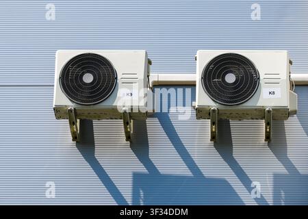 Two outdoor HVAC condenser units installed on an insulated metal facade provide efficient cooling and climate control for a commercial building Stock Photo