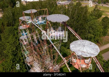 Aerial view of the abandoned Ferris wheel with weathered metal structures and colorful cabins surrounded by lush green trees in Elektrenai, Vilnius Co Stock Photo