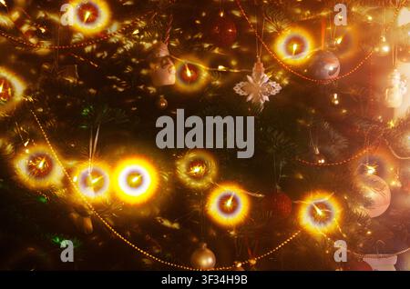 A closeup shot captures the enchanting glow of a decorated Christmas tree, adorned with various ornaments and bright, warm lights Stock Photo