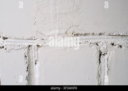 White painted block wall texture. White concrete bricks with messy mortar layers, uneven surface, and cracks in building construction Stock Photo