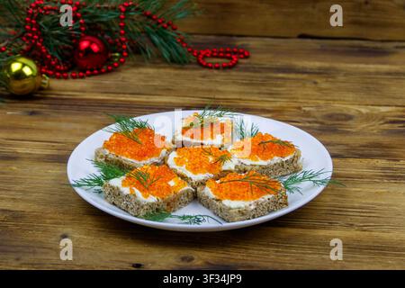Canapes with red caviar and Christmas decorations on wooden table Stock Photo