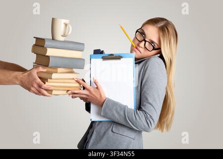 Stressed Young Businesswoman Juggling Books And Coffee In Office, Focused On Work Concept Stock Photo