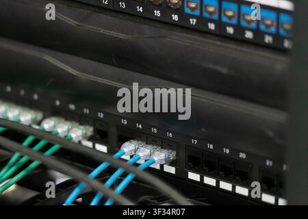 Close-up of blue and green patch cables connected to network equipment inside a telecommunications rack. Stock Photo