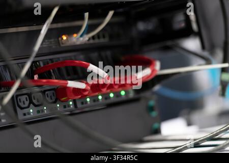 Close-up of red and white patch cables connected to rack-mounted network equipment with illuminated status indicators. Stock Photo