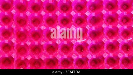 The bright pink texture of a paper egg tray, taken in close-up. A repeating geometric pattern of cells creates an abstract background with rich color and pronounced texture. The image is suitable for use in design, printing, packaging, modern backgrounds, decorative projects and environmental concepts of recycled materials Stock Photo
