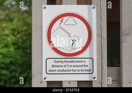 A white warning sign instructing people to keep a safety distance of at least 3 meters from the down conductor during a thunderstorm. Stock Photo