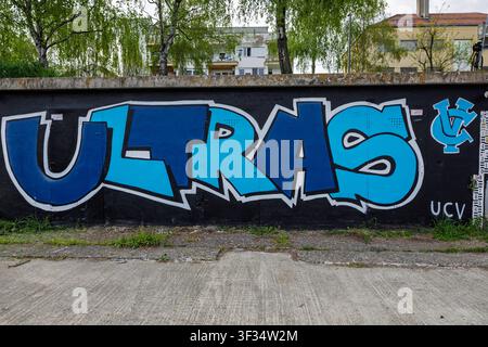 Vinkovci, Croatia - April 15.2026:Large blue "ULTRAS" graffiti mural painted on a black concrete wall in an urban neighborhood, framed by birch trees Stock Photo