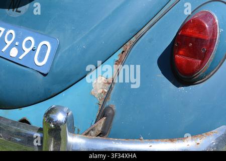 Rust and corrosion on the rear quarter panel of a classic blue Volkswagen Beetle, showing body deterioration and the need for restoration. Stock Photo