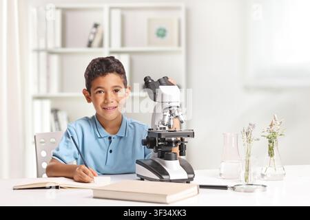 Boy doing biology research and writing on a desk with a microscope Stock Photo