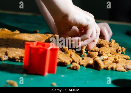 Child Making Gingerbread Cookies with Red Cookie Cutter on Green Table Stock Photo