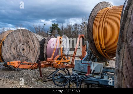 Large wooden spools of orange and pink cables on construction trailers under a cloudy sky, ready for utility installation Stock Photo