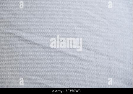 White Textured Cotton Fabric Texture with Soft Folds Background. High quality photoClose-up view of soft crumpled white woven fabric texture showing rich pattern detail, natural folds, and soft shadows. Ideal background for fashion, textiles, martial arts gi fabric, minimalist design, or apparel concepts. Stock Photo