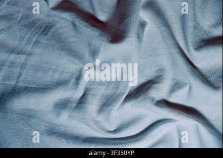 Blue Textured Cotton Fabric Background with Crumpled Soft Folds. High quality photoClose-up full frame view of light blue knitted or woven fabric texture with natural soft folds and shadows. Modern abstract background suitable for fashion, textile concepts, sportswear, banner design, or apparel mockup. Stock Photo