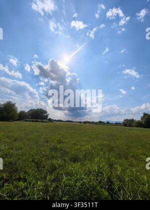Sun rays breaking through dramatic summer clouds above a green meadow in Hesse, Germany. Stock Photo