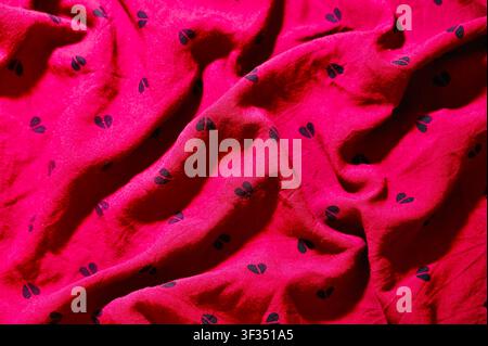 Red Fabric with Heart Close-up of crumpled red fabric featuring small black heart prints. Soft folds and dynamic shadows create a cozy and romantic texture. Ideal background for Valentine's Day, love concepts, fashion design, or textile mockups. Background with Soft Waves. High quality photo Stock Photo