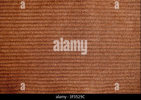 Close-up macro background texture of soft brown ribbed corduroy velvet fabric with fine vertical lines. Perfect for fashion design, textile background, tailoring, garment material, autumn style, and upholstery concepts. Stock Photo