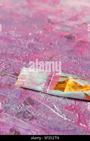 Pearlescent metallic acrylic paint mixed on a board with a used artist paint brush. Art and craft special effect paint supplies. Stock Photo