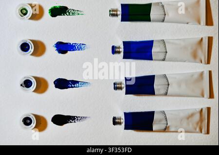 Colorful Acrylic Paint Tubes with Caps and Swatches on White Paper. High quality photoFlat lay top view of vibrant oil or acrylic paint tubes lined up with open caps and colorful paint swatches on white watercolor paper. Perfect for art, creativity, painting, art supply store, design background, and educational concepts. Stock Photo