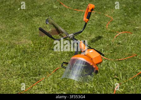 Grass trimmer and protective face shield on lawn Stock Photo