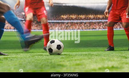 Lower body view of soccer players in red and blue uniforms dribbling each other for ball possession, running across pitch during match play. Footballers in motion blur. Stock Photo