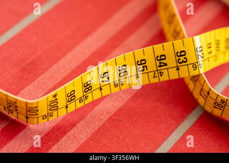 Close up view of a yellow measuring tape curled on a red striped fabric background Stock Photo
