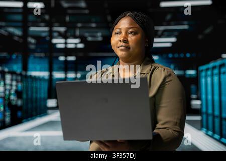 Software developer uses laptop in sustainable data center, implementing green technologies. African american IT expert working on energy efficient solutions to reduce server hub carbon footprint Stock Photo