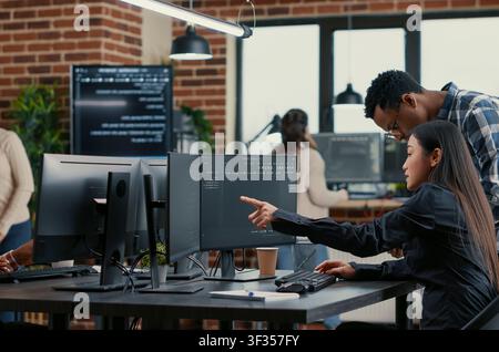Collaborative team of software developers reviewing source code pointing around computer screens, showing developer teamwork, source code discussion and cloud programming workflow. Stock Photo